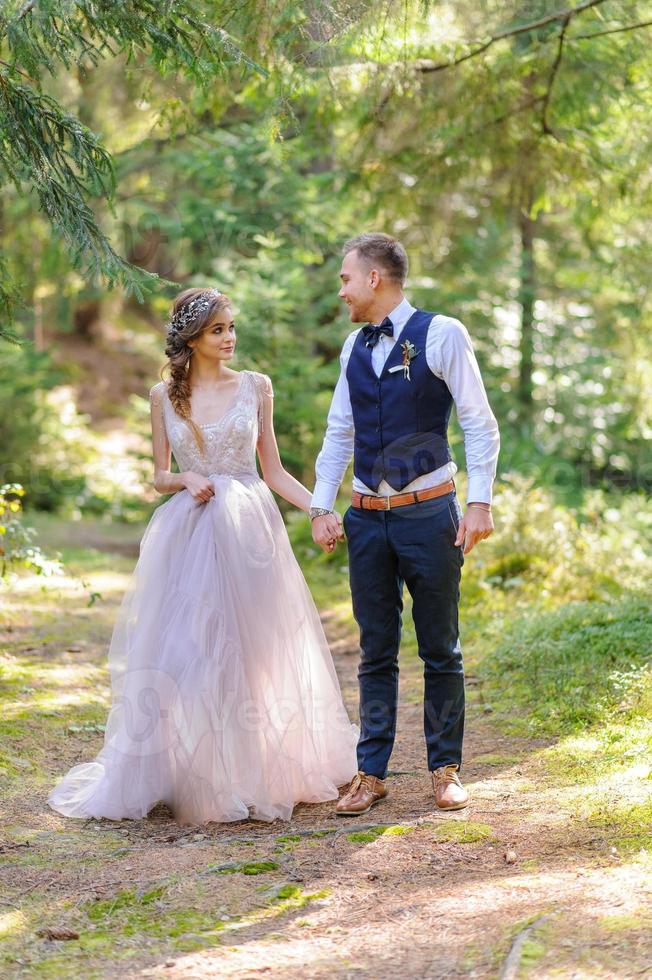 um atraente casal recém-casado, um momento feliz e alegre. um homem e uma mulher se barbeiam e se beijam com roupas de férias. cerimônia de casamento de estilo boêmio na floresta ao ar livre. foto