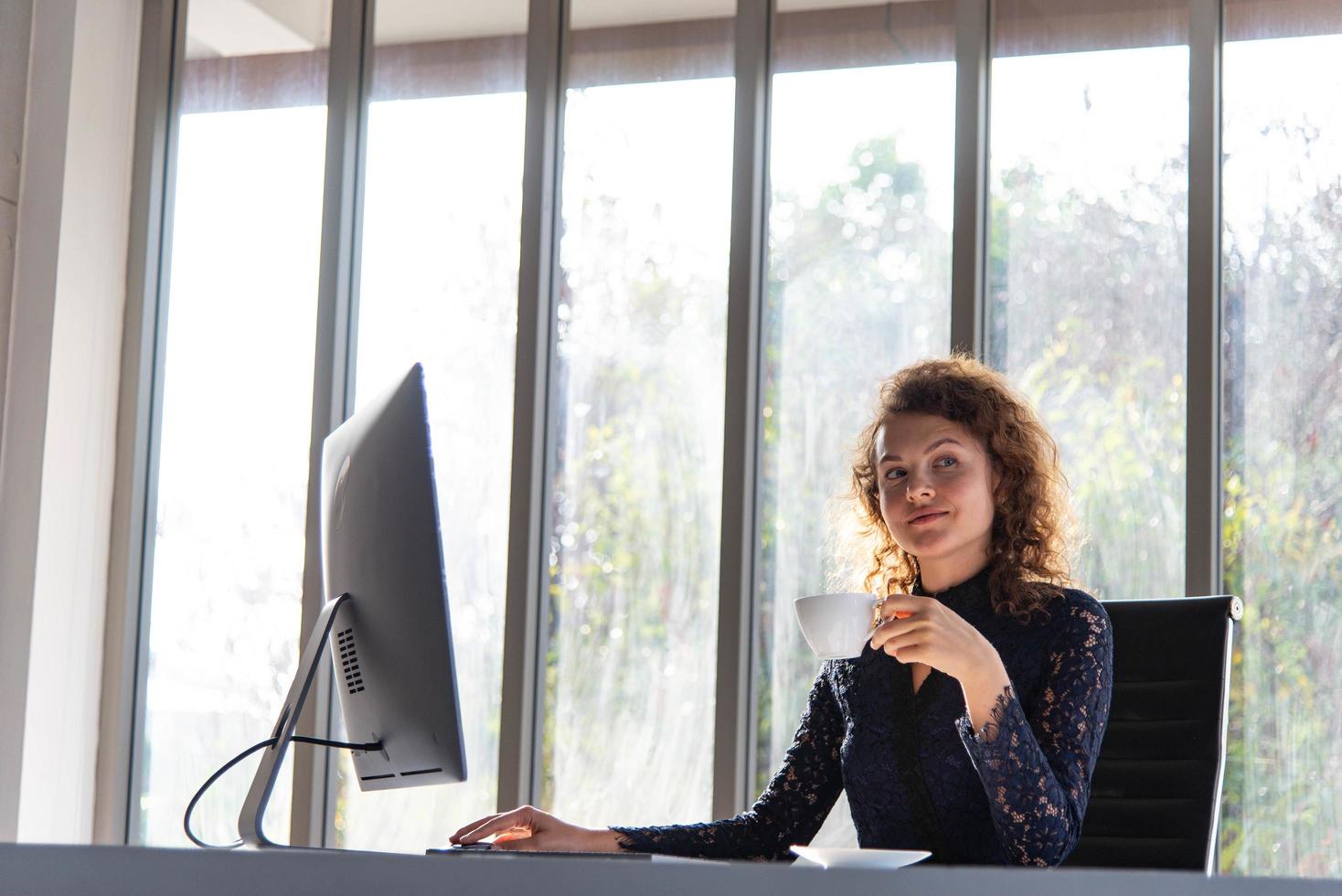 mulher de negócios bonita e confiante atraente trabalhando com computador e tomando café no escritório moderno ou em casa foto