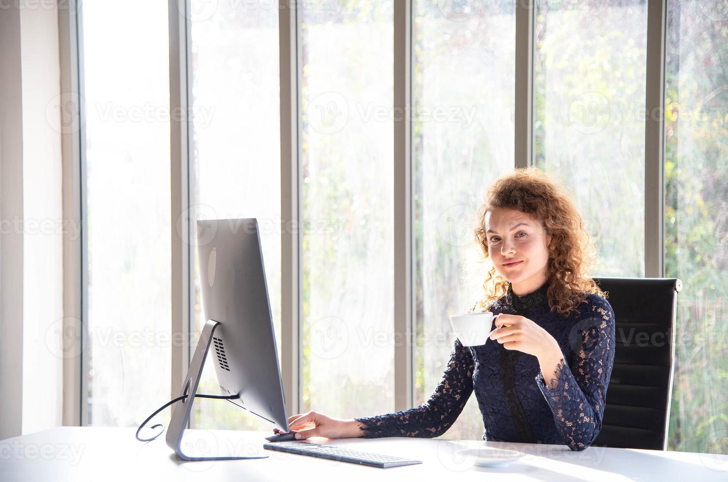 mulher de negócios bonita e confiante atraente trabalhando com computador e tomando café no escritório moderno ou em casa foto