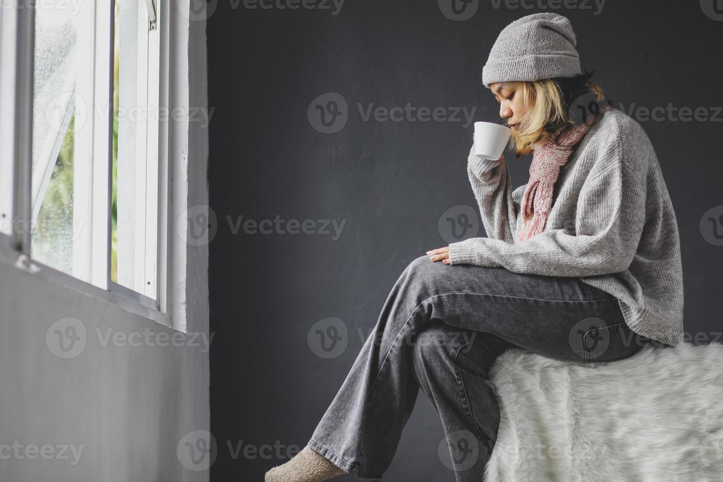 garota solitária sentada e bebendo uma xícara de café na frente da janela na temporada de inverno foto