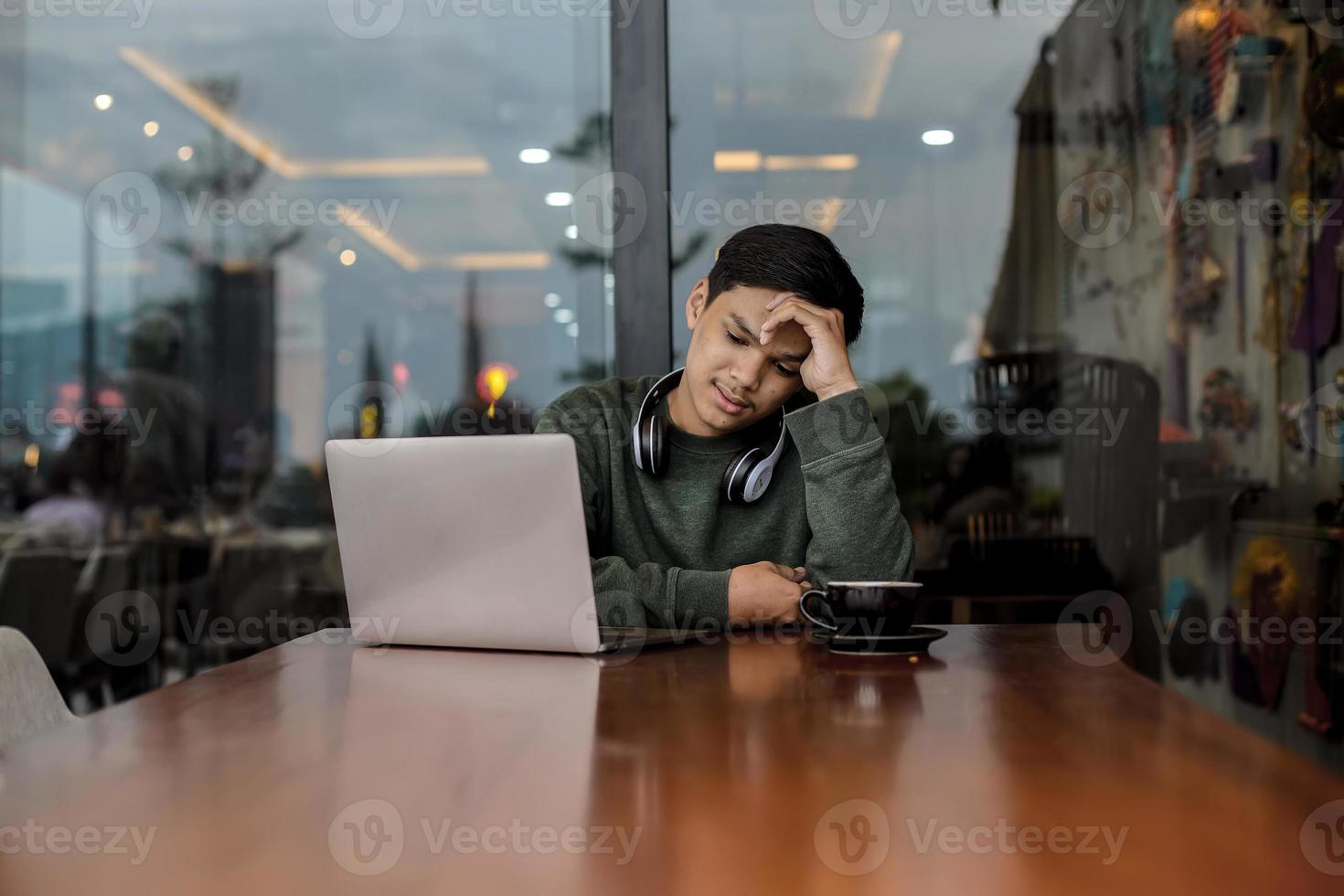 estudante universitário masculino asiático confuso enquanto estudava usando um laptop no café ou cafeteria foto