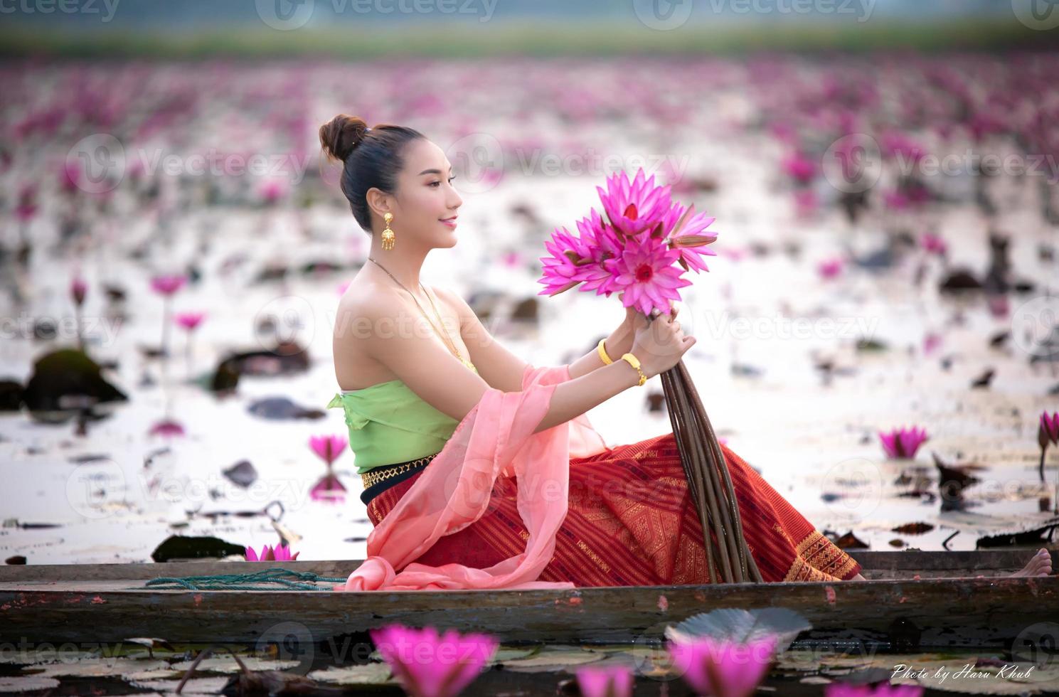 jovens mulheres asiáticas em trajes tradicionais no barco e flores de lótus rosa na lagoa foto