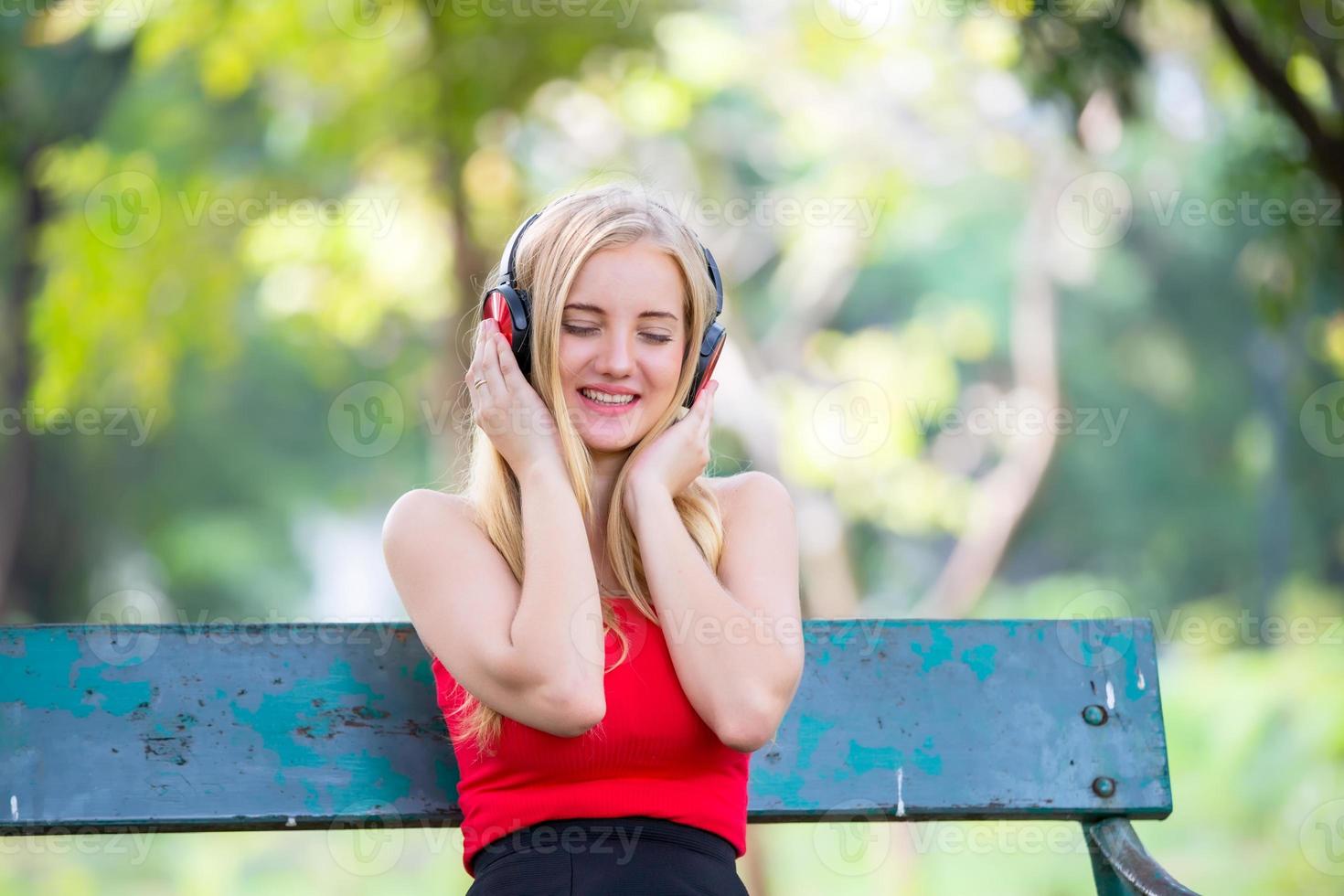 linda mulher loira em pé enquanto ouve música no fone de ouvido no parque. foto