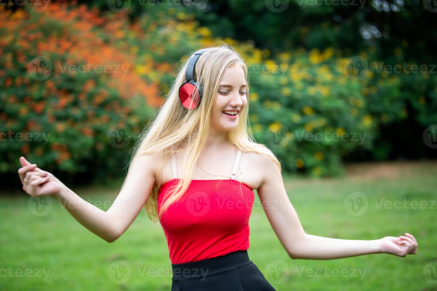 linda mulher loira em pé enquanto ouve música no fone de ouvido no parque. foto