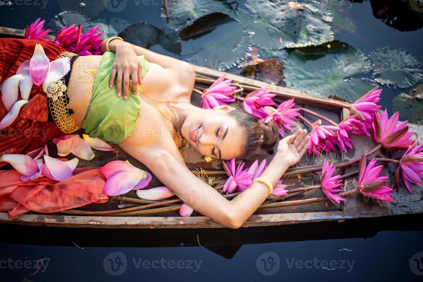 jovens mulheres asiáticas em trajes tradicionais no barco e flores de lótus rosa na lagoa foto