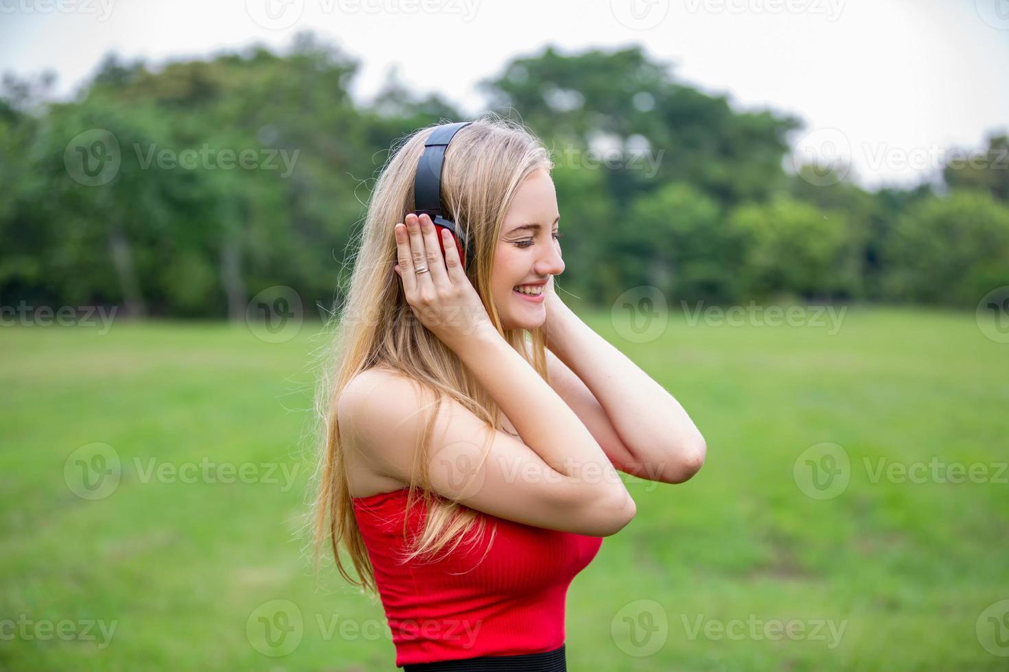 linda mulher loira em pé enquanto ouve música no fone de ouvido no parque. foto