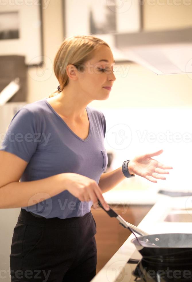 retrato de vista lateral de mulheres em seu jantar de pé ao lado do fogão e cozinhando em uma parede de azulejos brancos de fogão a gás com luz quente foto