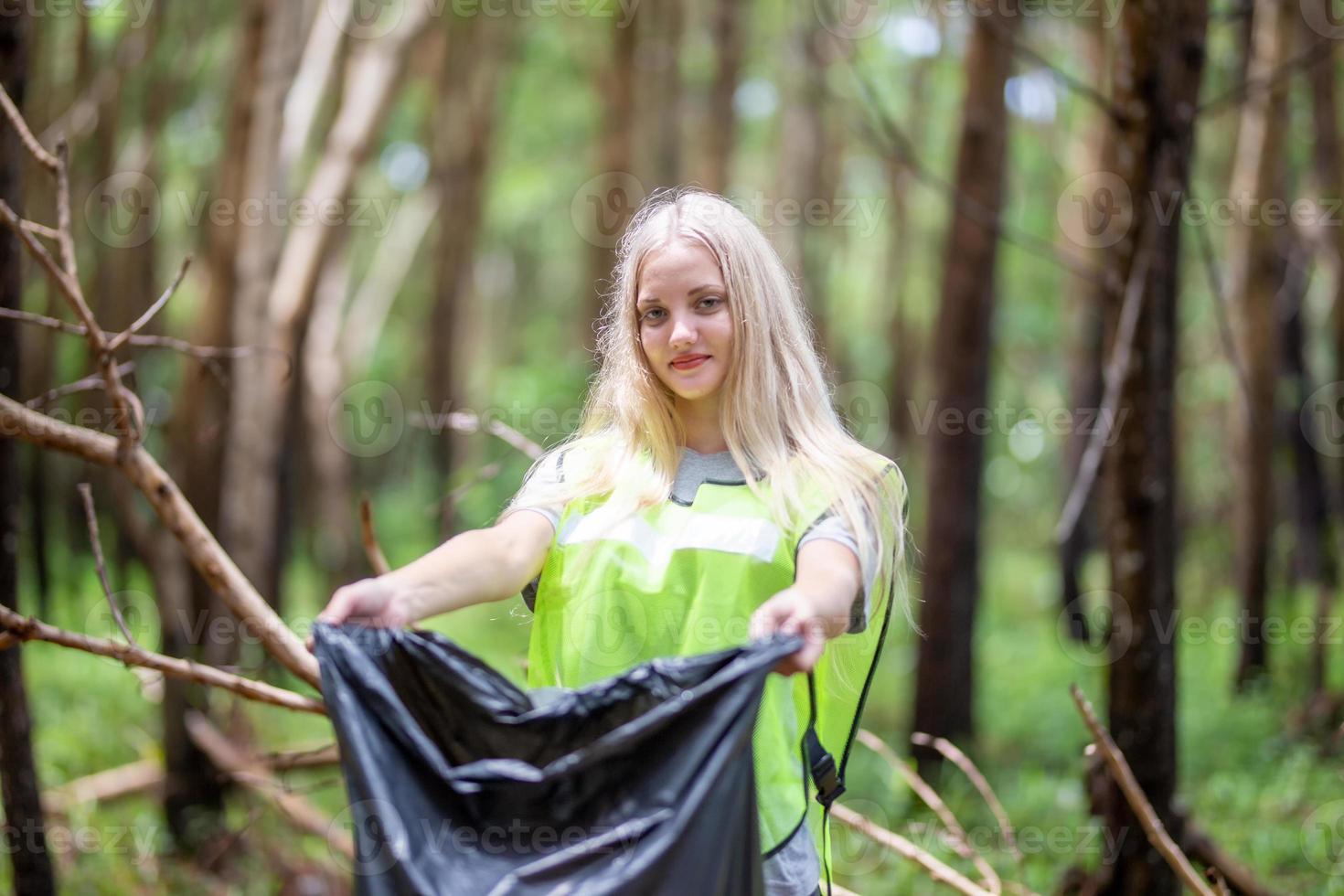 uma linda mulher se voluntaria para segurar um saco de lixo preto para coletar lixo. foto