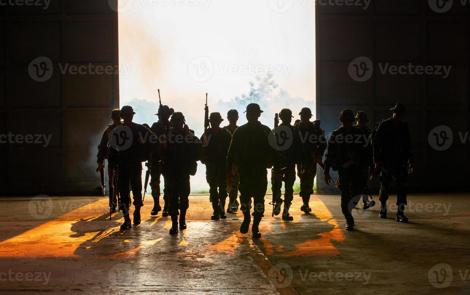 silhuetas de soldados do exército no nevoeiro contra um pôr do sol, equipe de fuzileiros navais em ação, cercado de fogo e fumaça, atirando com rifle de assalto e metralhadora, atacando inimigo foto