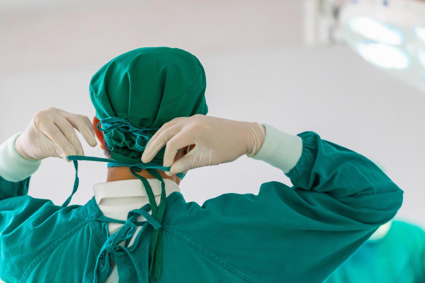 vista traseira do cirurgião amarrando a tampa cirúrgica em preparação, equipe médica realizando operação cirúrgica na sala de cirurgia, cirurgião da equipe no trabalho na sala de cirurgia foto