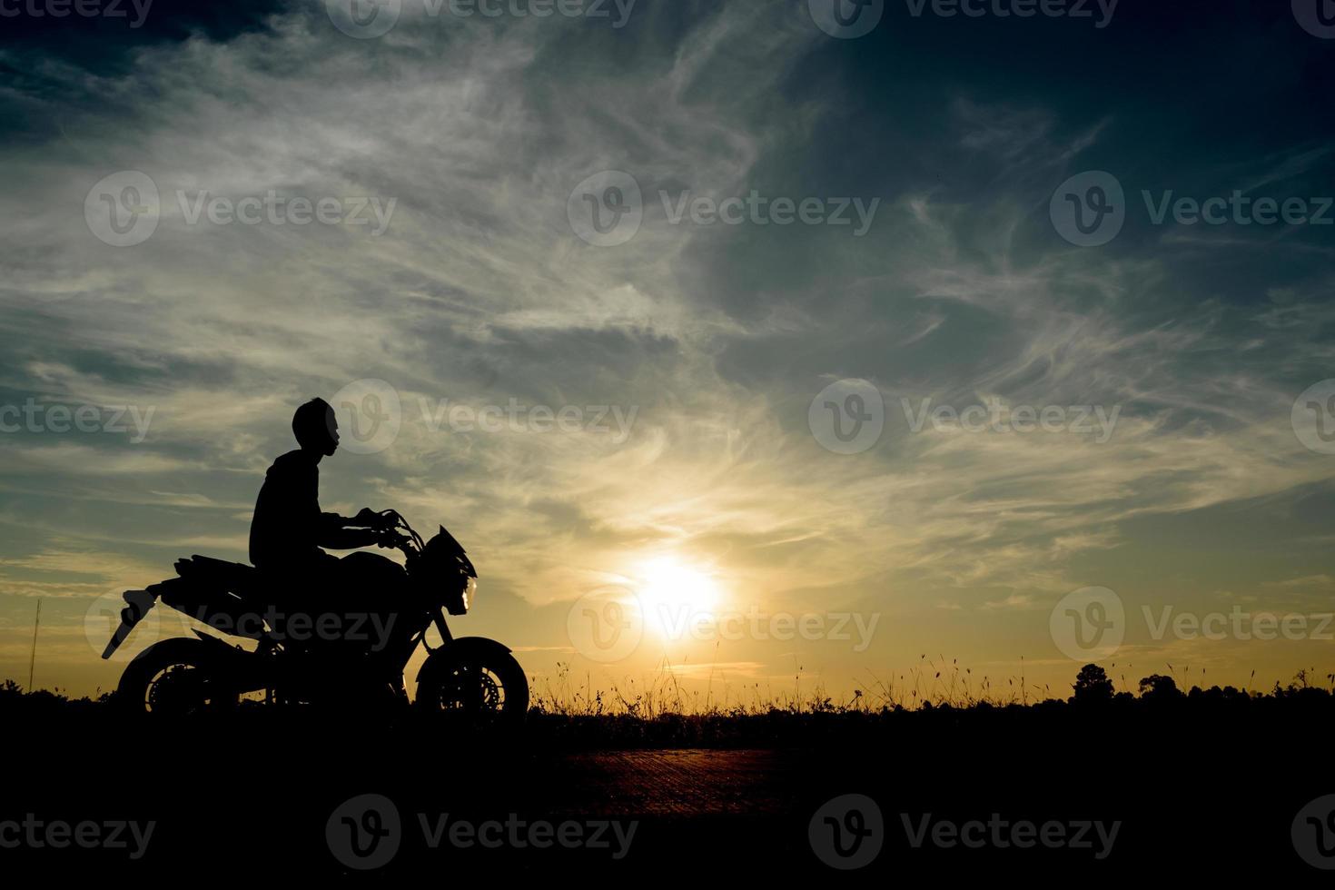 imagem de silhueta de um homem viajar de moto ao pôr do sol com fundo de céu laranja-azul foto