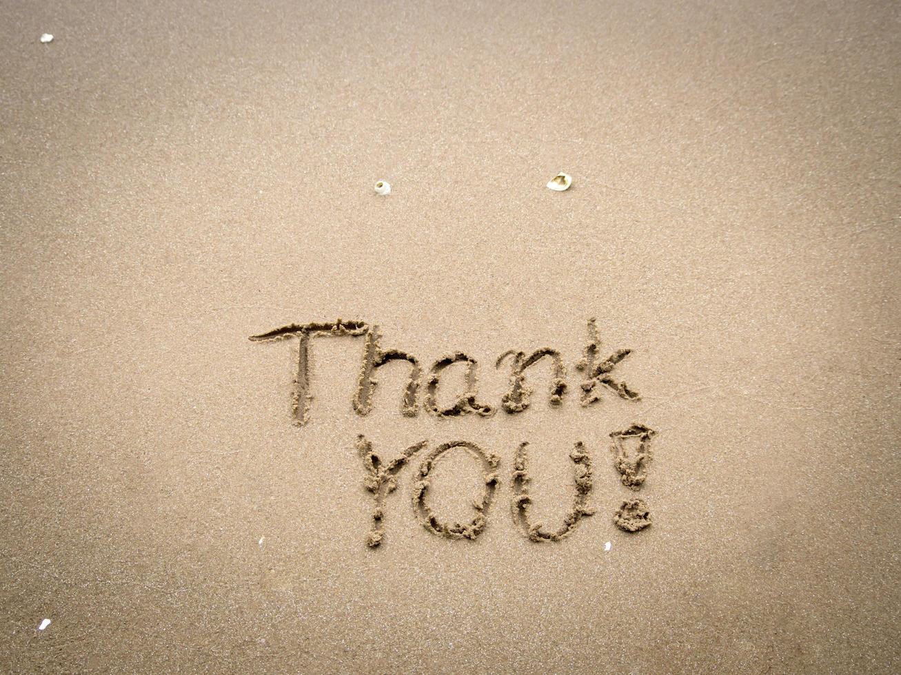 obrigado pelas palavras escritas ou desenhadas na areia limpa da praia com céu azul pela manhã. foto