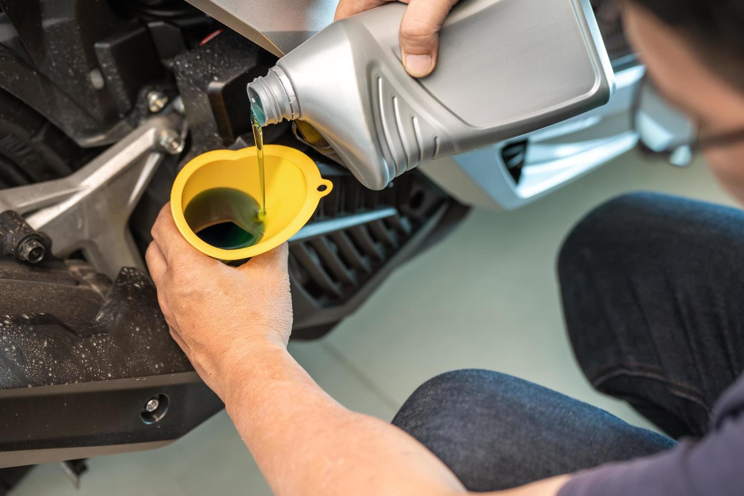 mecânico de motocicleta derramando óleo na scooter do motor. conceito de motocicleta de manutenção e reparação na garagem foto