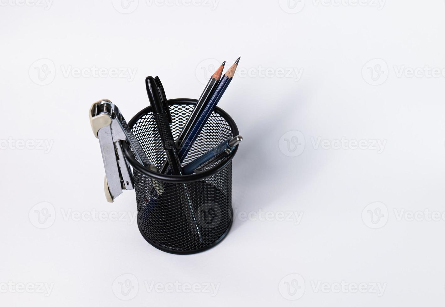 uma pequena cesta preta feita de aço redondo. pode ser usado para guardar material de escritório, incluindo canetas, lápis, grampeador, e ainda tem espaço para colocar mais coisas. no fundo branco há espaço de cópia. foto