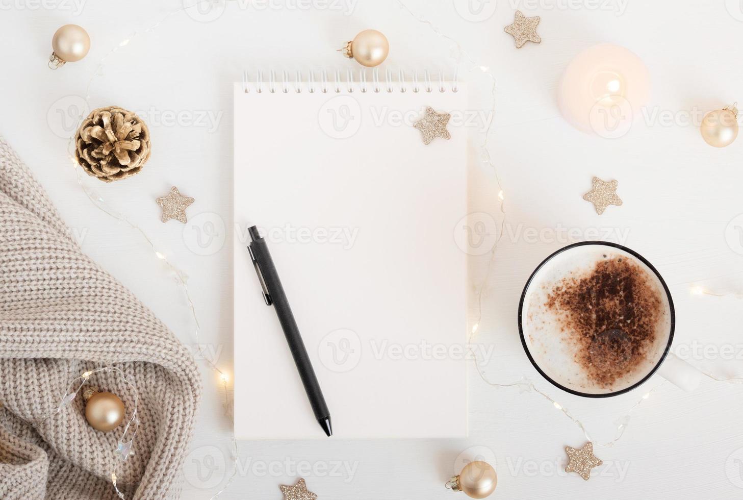 folha branca de caderno com caneta na mesa branca com xícara de cacau ou café, vela e guirlanda festiva. planejamento de conceito, lista de desejos para o ano novo. maquete para letras, desenho de arte. foto