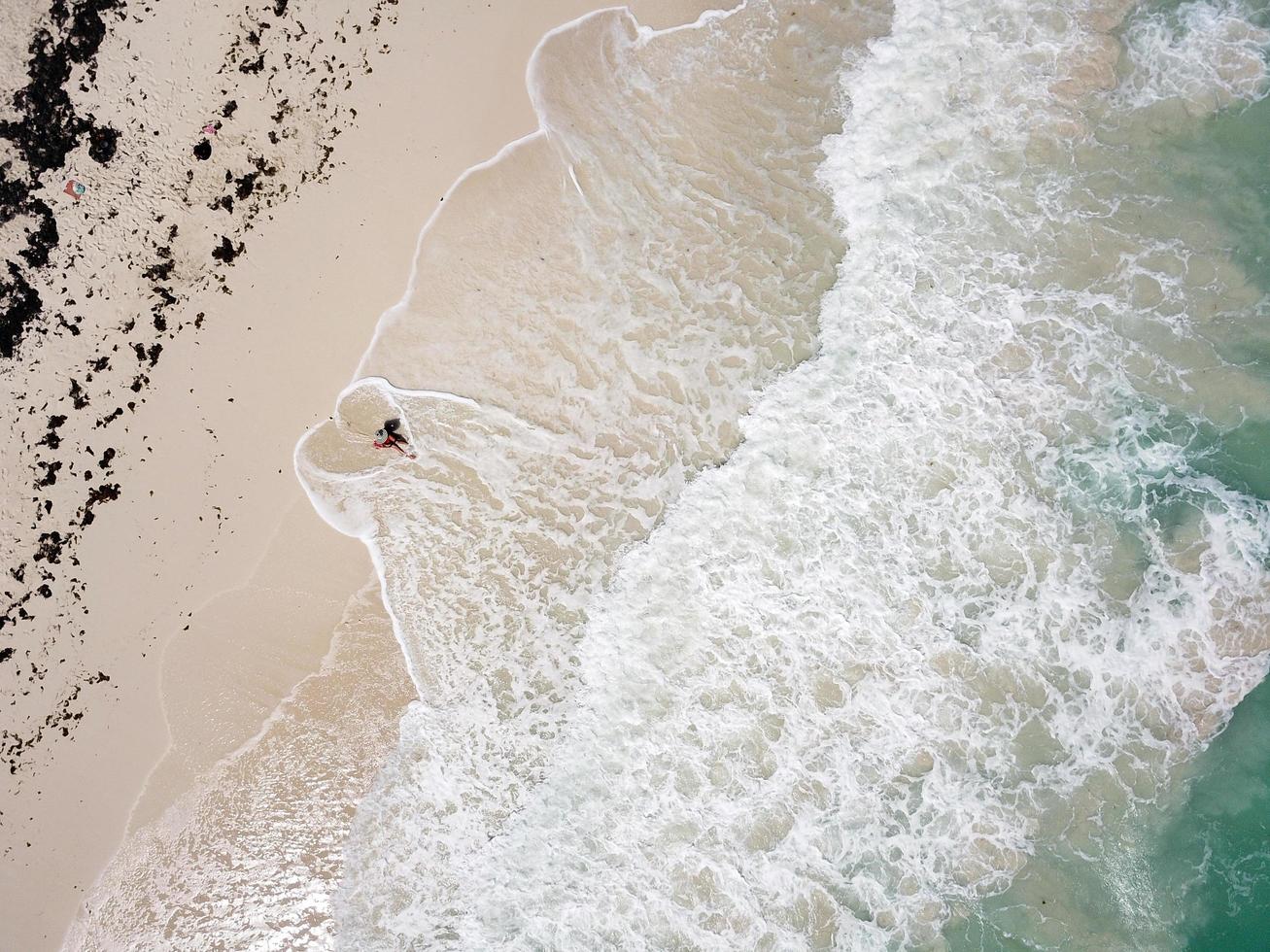 vista aérea da praia, ondas fazendo formato de coração em torno de uma mulher de chapéu foto