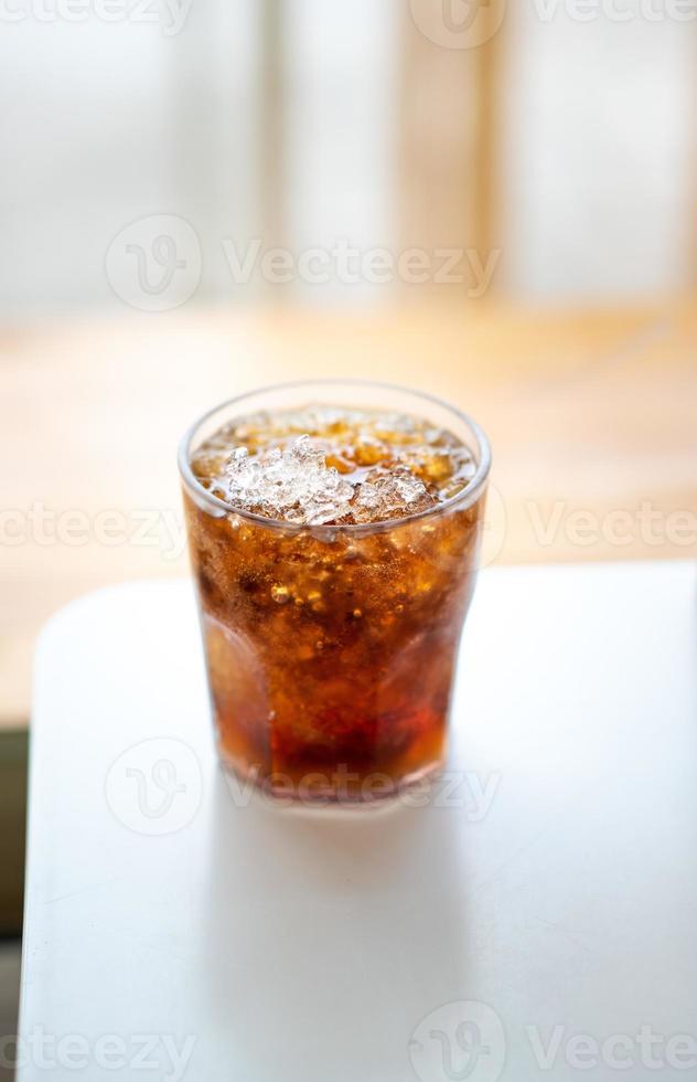 refrigerante com gelo em um copo em uma mesa branca foto