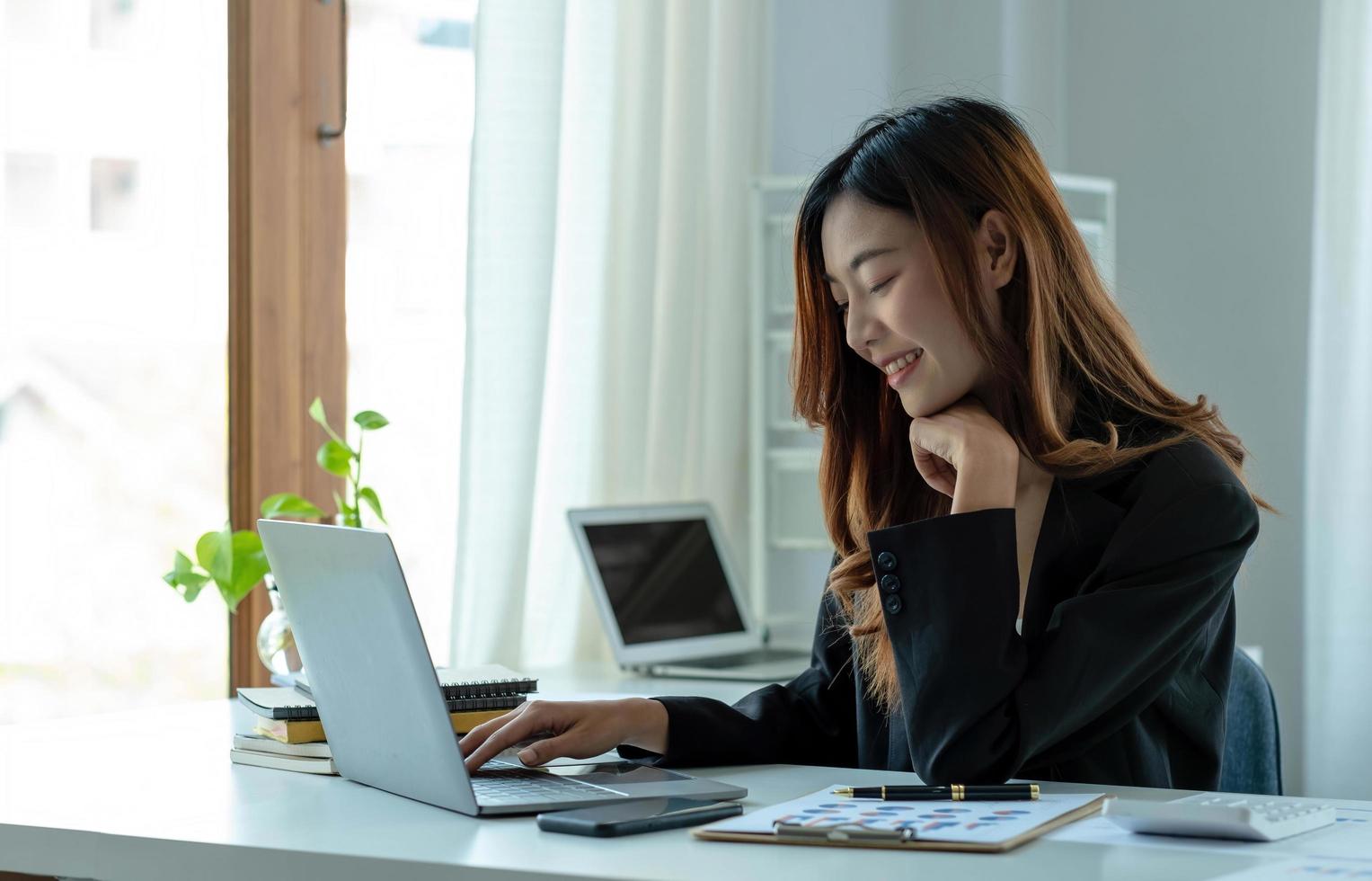 feliz jovem empresária asiática sentada em seu local de trabalho no escritório. jovem trabalhando no laptop no escritório. foto