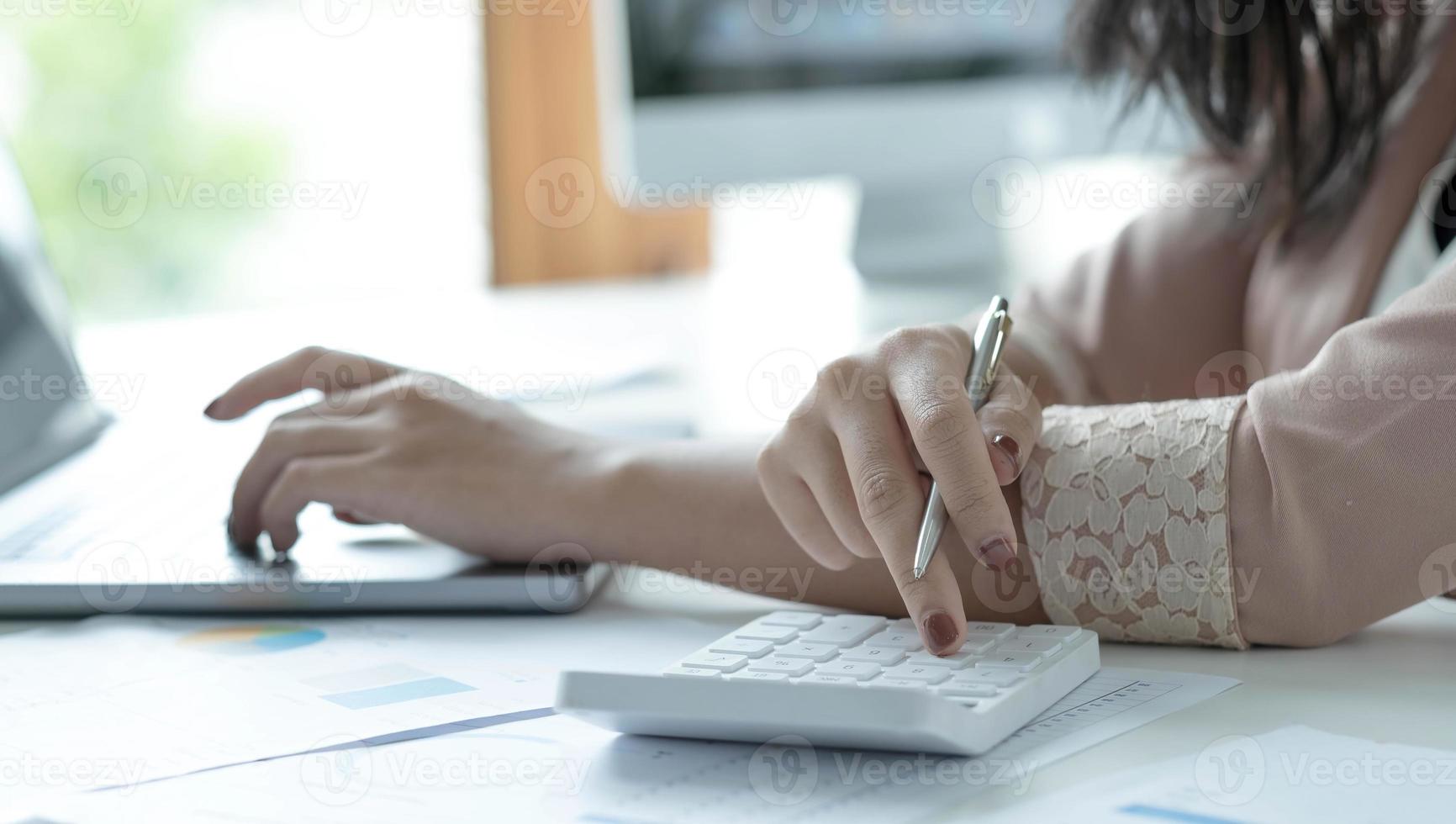 contador de mulher usa calculadora e computador na mesa no escritório. trabalhar com segurança em casa. conceito de finanças e contabilidade foto