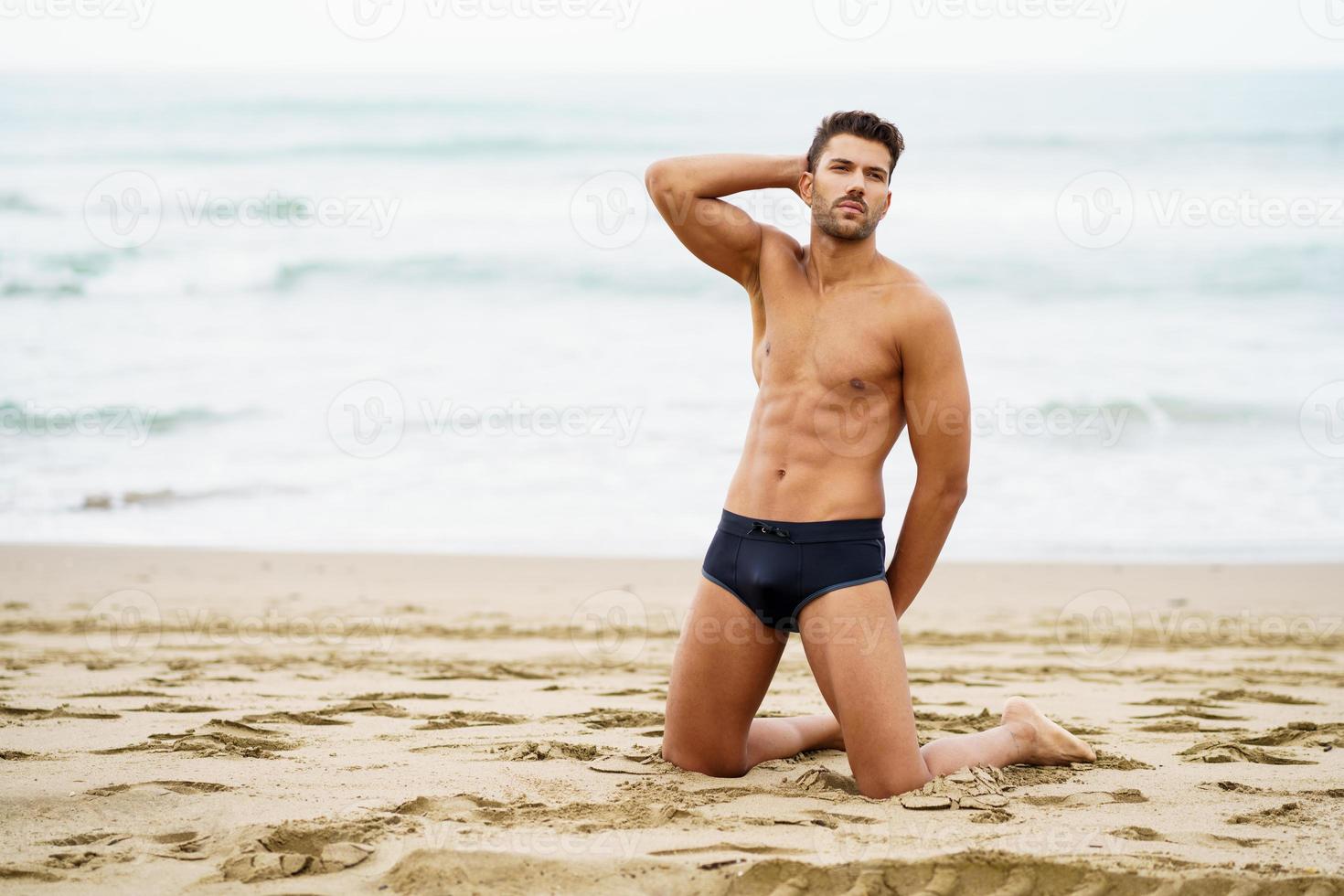 homem bonito de joelhos na areia da praia foto