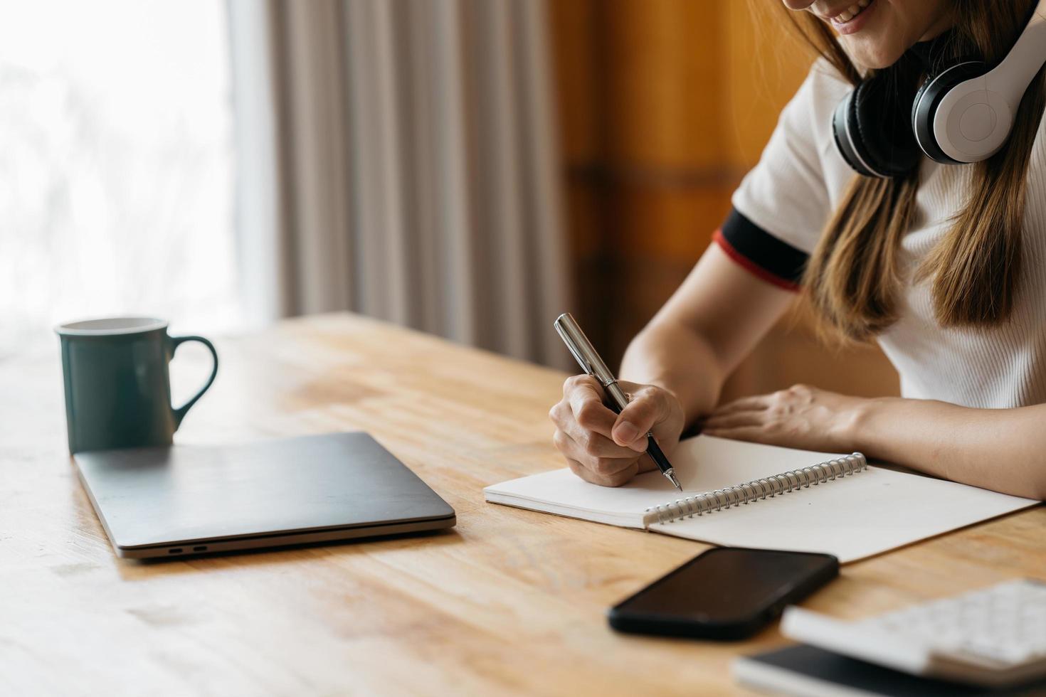 feliz asiático no uso de fone de ouvido laptop fazer treinamento de curso on-line fazer anotações. sorrindo jovem estudante asiática em fones de ouvido estuda no computador em casa. conceito de educação a distância. foto