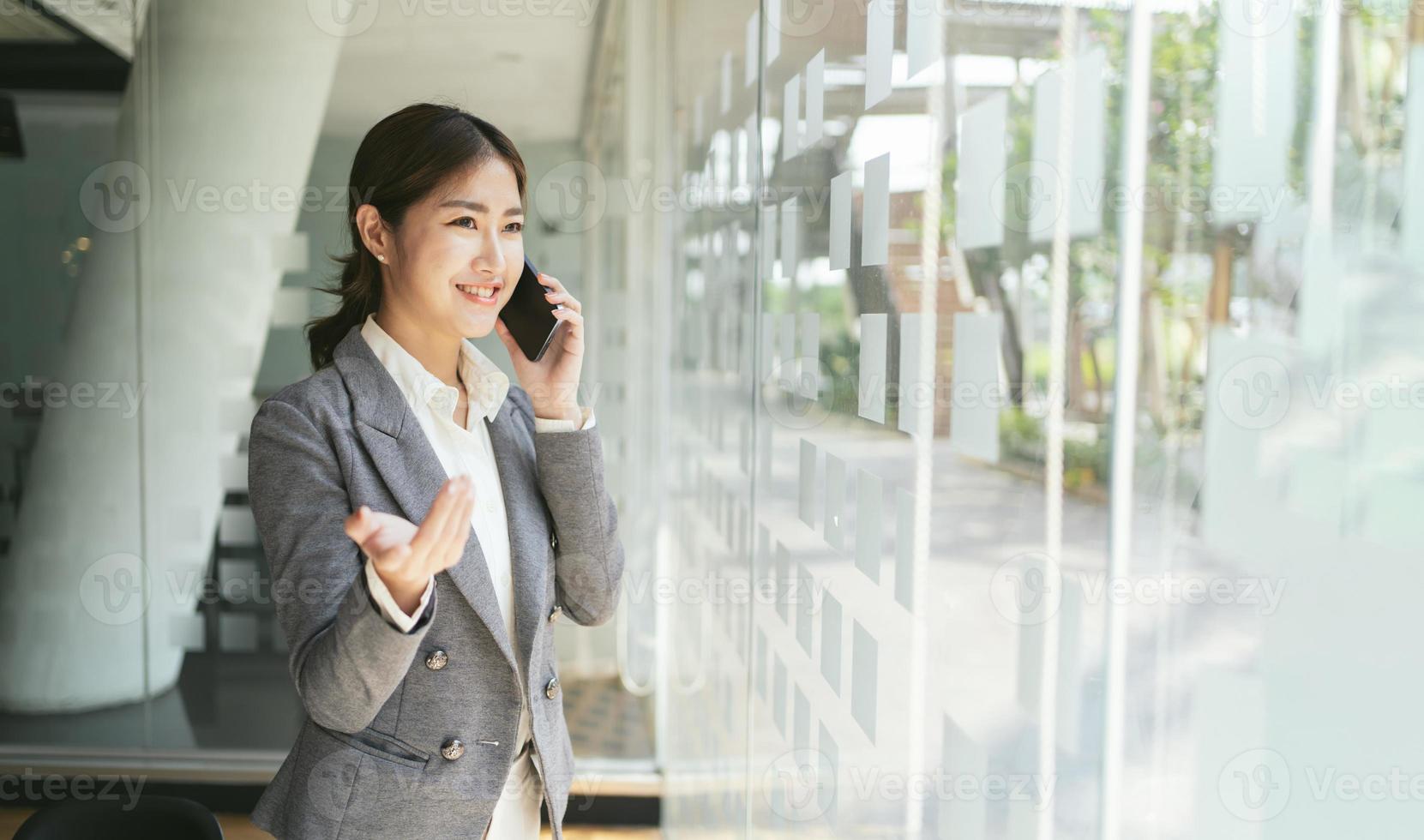 mulher asiática com smartphone em pé no fundo do escritório moderno e espaço de cópia, foto de negócios de moda de linda garota de terno casual com telefone inteligente.