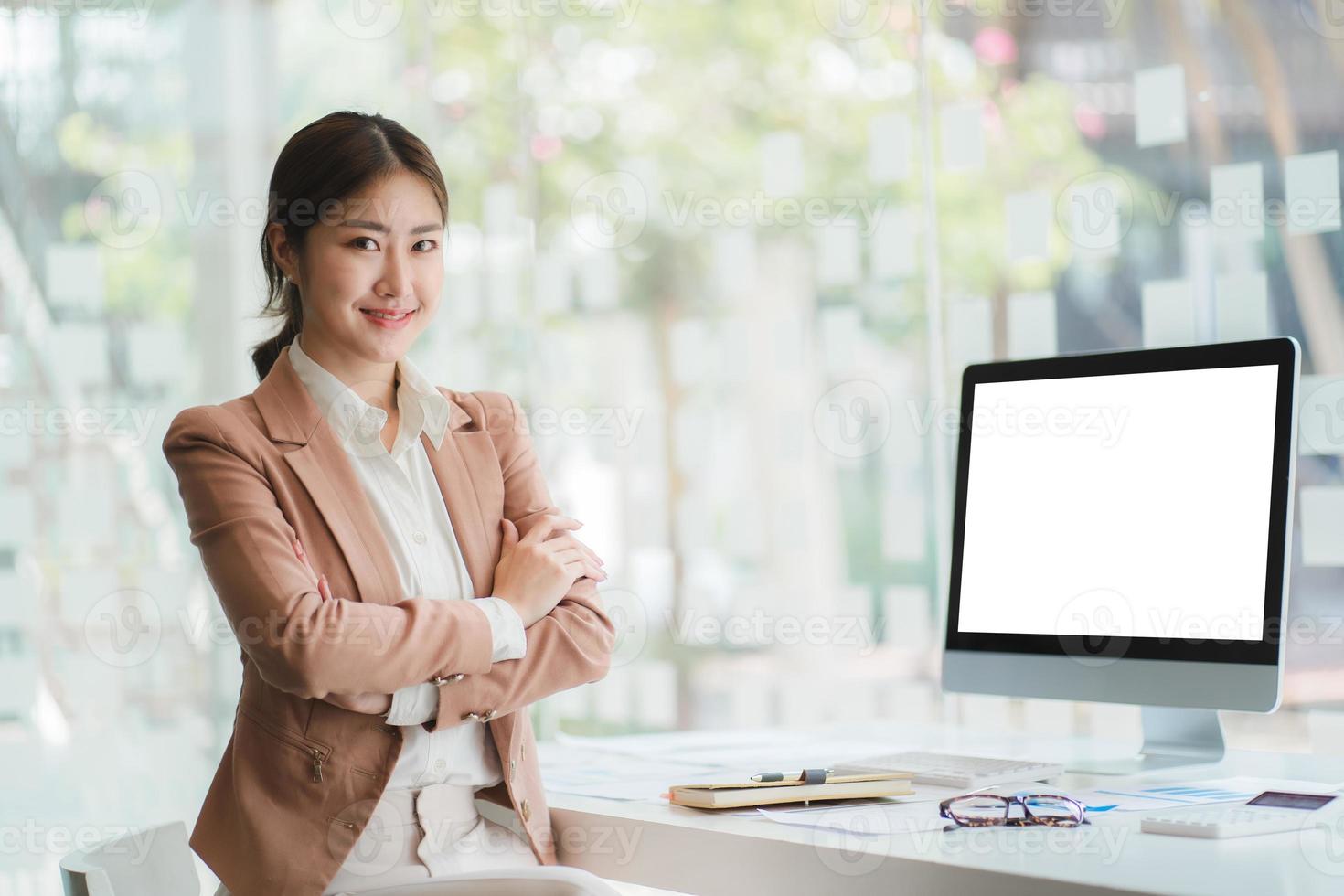 linda mulher asiática sorridente trabalhando no escritório, olhando para a câmera. com tela em branco do computador. foto