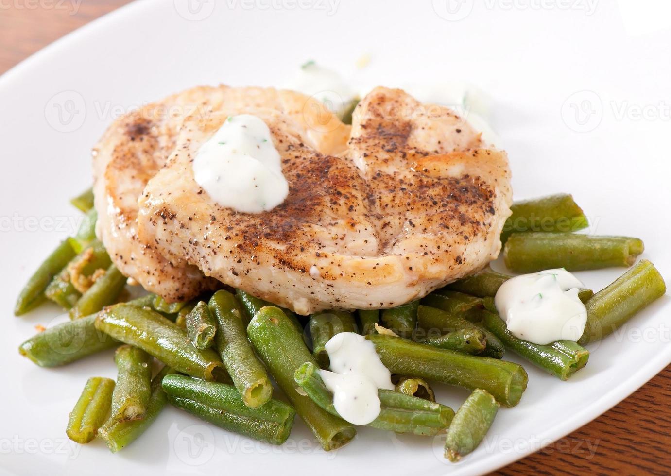 peito de frango grelhado com feijão verde e molho num prato branco. foto