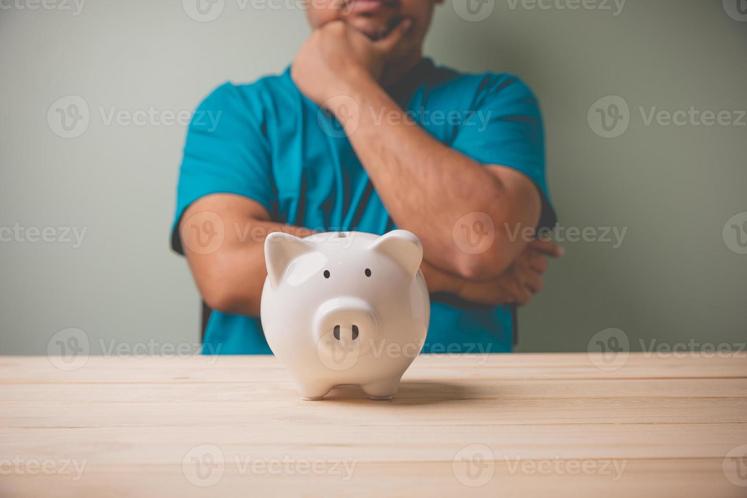 um cofrinho branco em uma mesa de madeira com um homem considere um cofrinho branco para planejar economizar dinheiro para uso futuro de investimento. economia de conceito, planejamento financeiro para o futuro, negócios, contabilidade. foto