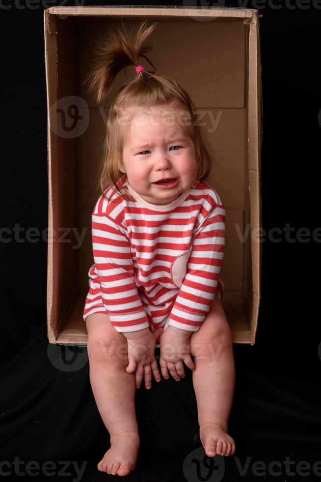 menina bonitinha e linda senta-se em uma caixa. foto