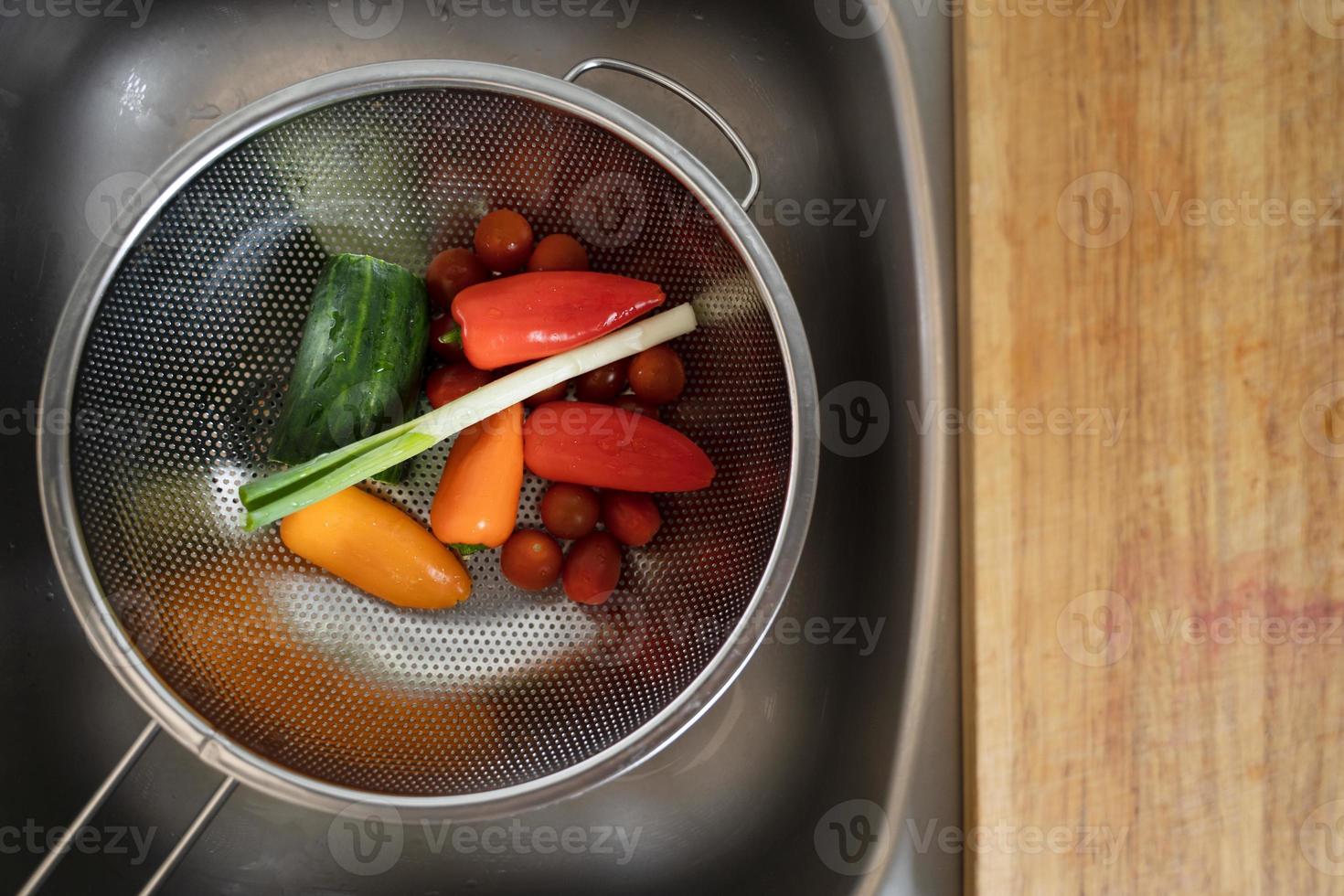 pepino tomate cebola verde e pimentão em uma peneira na pia da cozinha foto