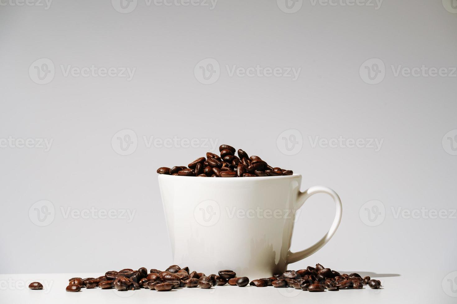 grãos de café em xícara no fundo branco foto