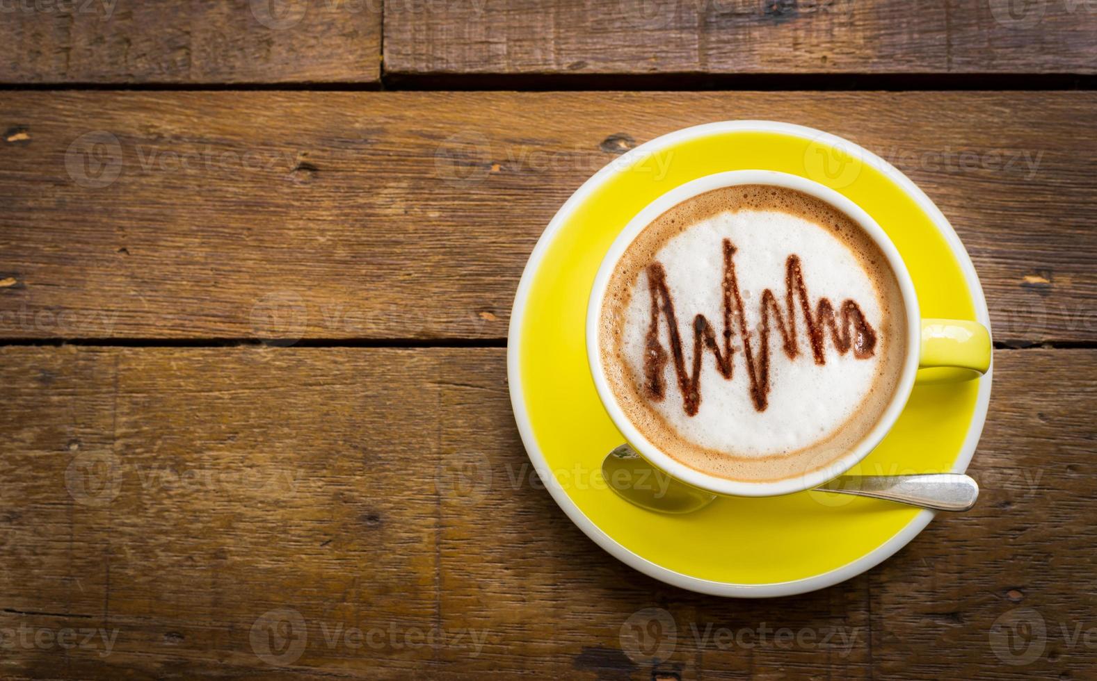 vista superior do café com leite ou café cappuccino em copo amarelo com latte art na mesa de madeira. foto