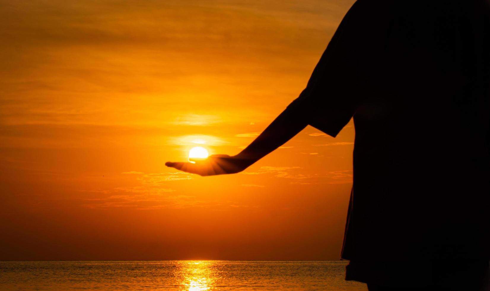 silhueta de uma garota levantando a mão, coloque o sol, coloque-o na palma da sua mão. pelo mar. sol da manhã. no mar. tons claros de laranja. foto