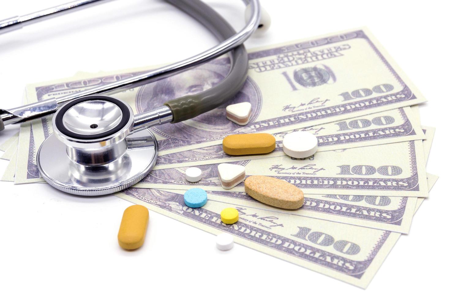 estetoscópio com banco de dólares e cápsulas de remédios em fundo branco. estilo de vida saudável com conceito de finanças empresariais foto