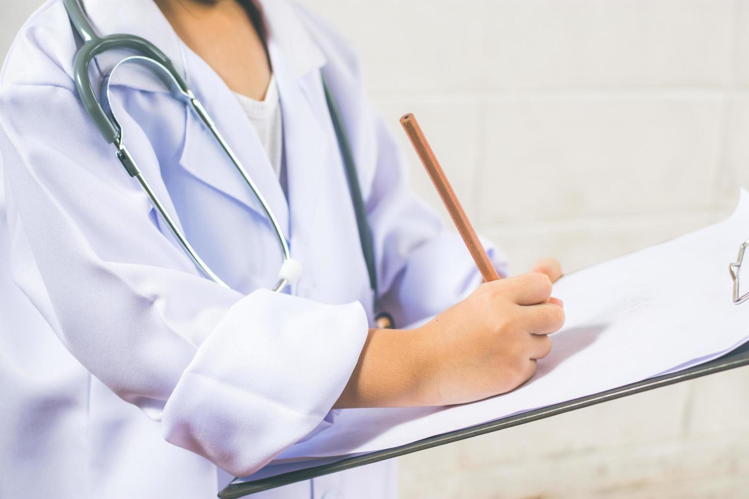 menina asiática vestindo como um médico escrevendo prescrição e preparando o relatório de pacientes foto