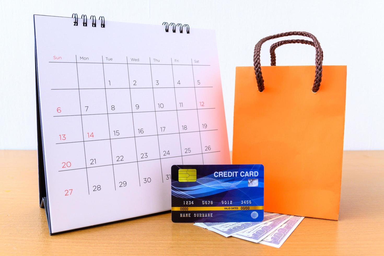 calendário com dias e cartão de crédito e saco de papel laranja na mesa de madeira. conceito de compras foto