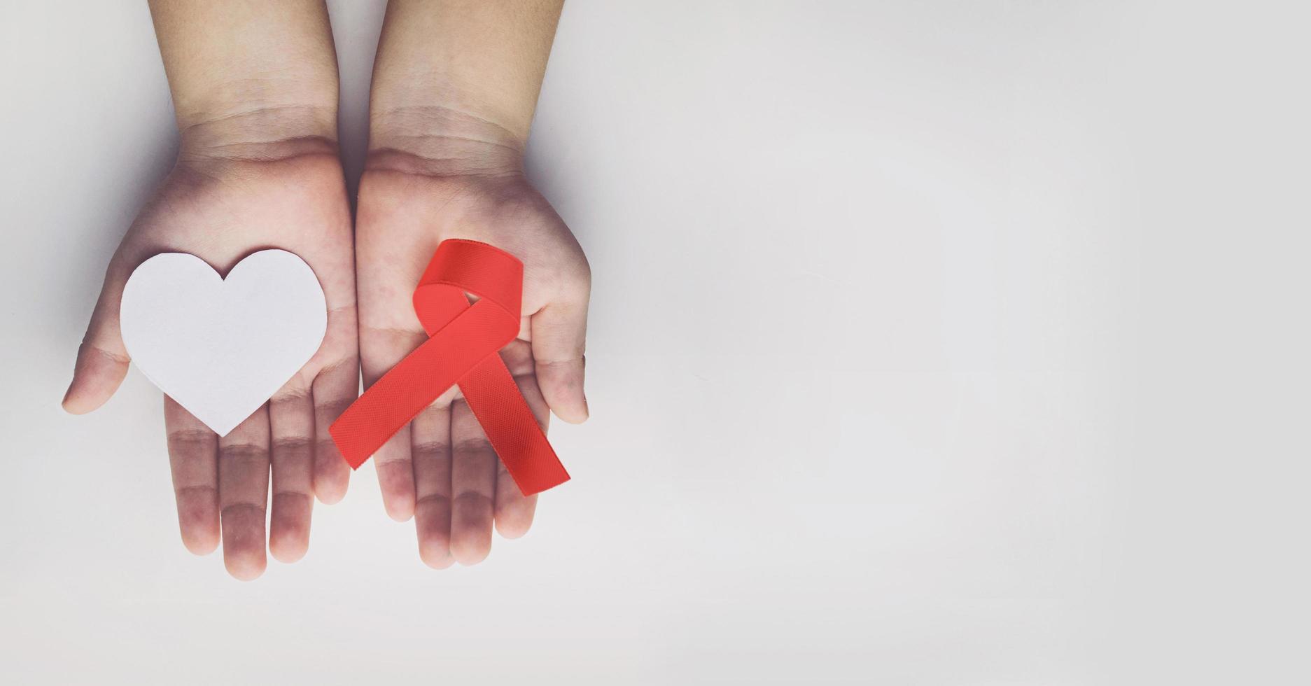 mãos de criança segurando a fita vermelha de conscientização da aids. ajuda na conscientização foto