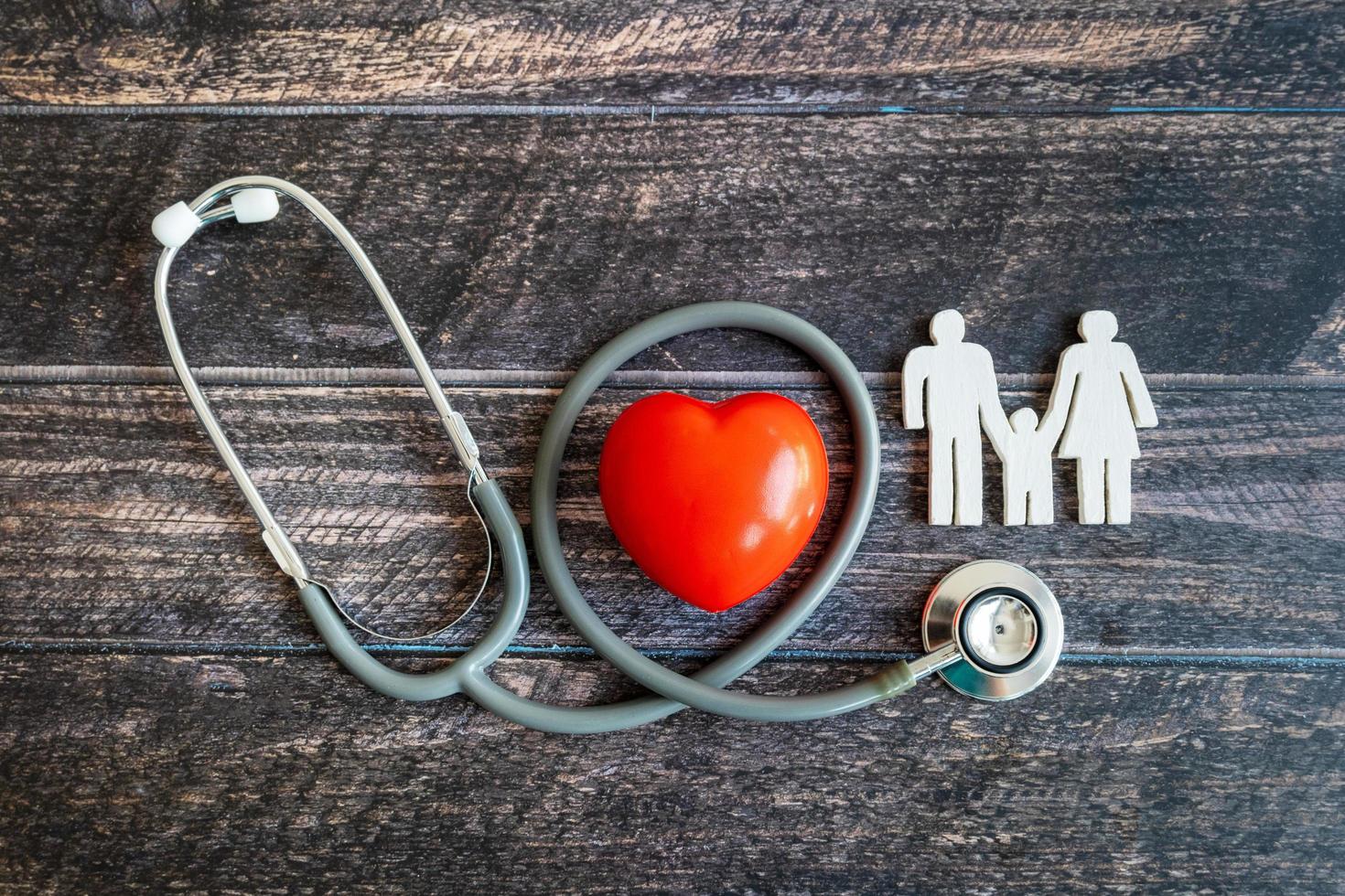 coração vermelho, estetoscópio e família de ícones na mesa de madeira. conceito de seguro médico foto