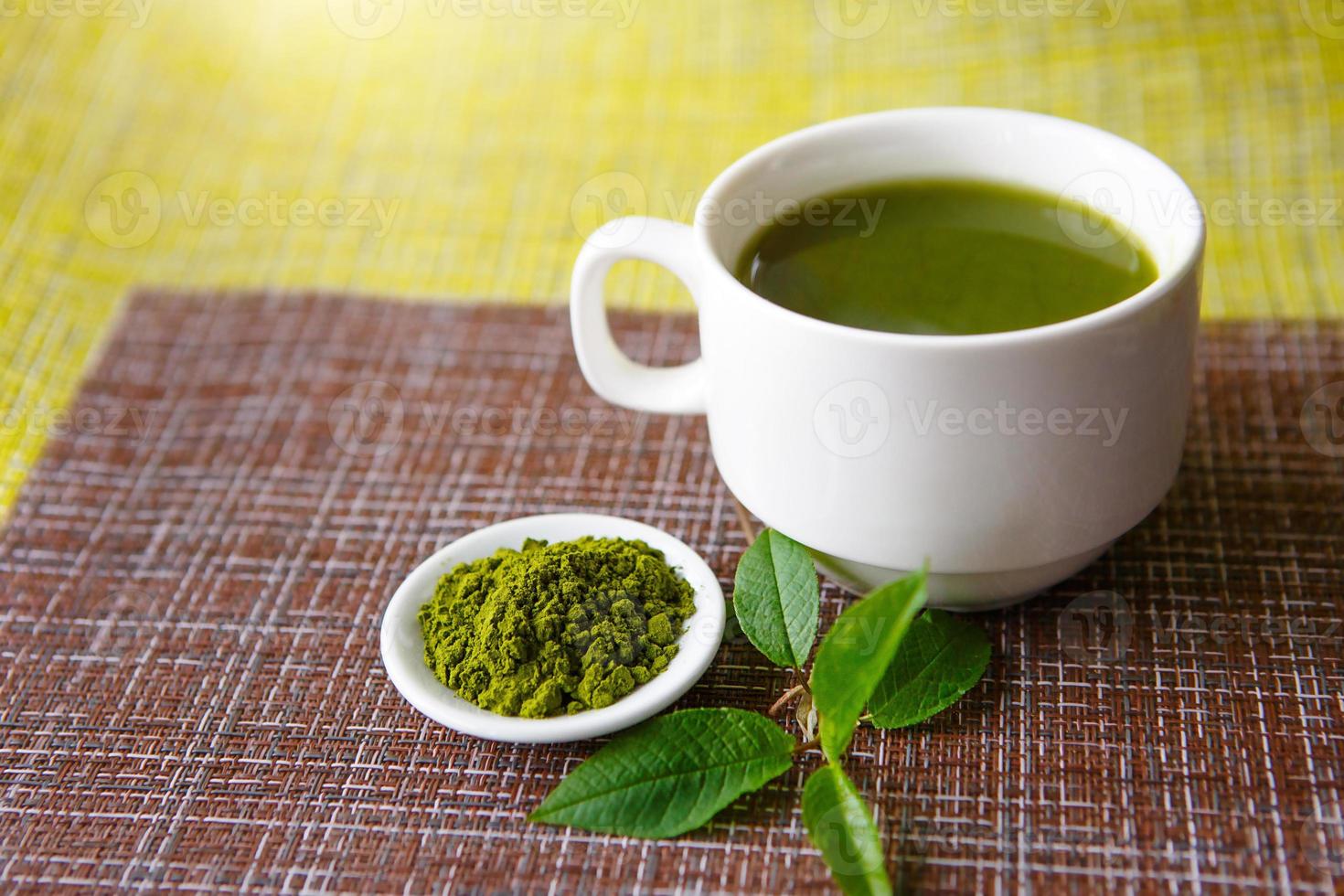 chá verde matcha japonês é derramado em uma caneca branca e em um pires branco em pó. chá definido em um guardanapo texturizado de flores naturais, decorado com um ramo de folhas verdes. copo com maquete foto