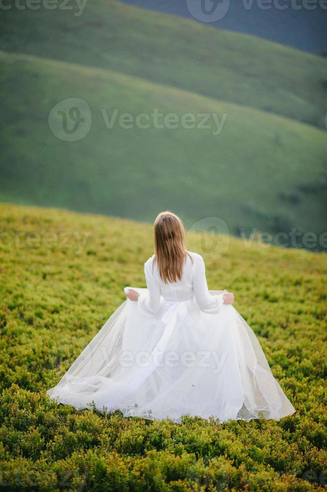 mulher em um vestido de noiva atravessa o campo em direção às montanhas foto