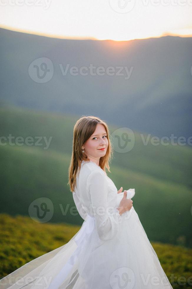 mulher em um vestido de noiva atravessa o campo em direção às montanhas foto