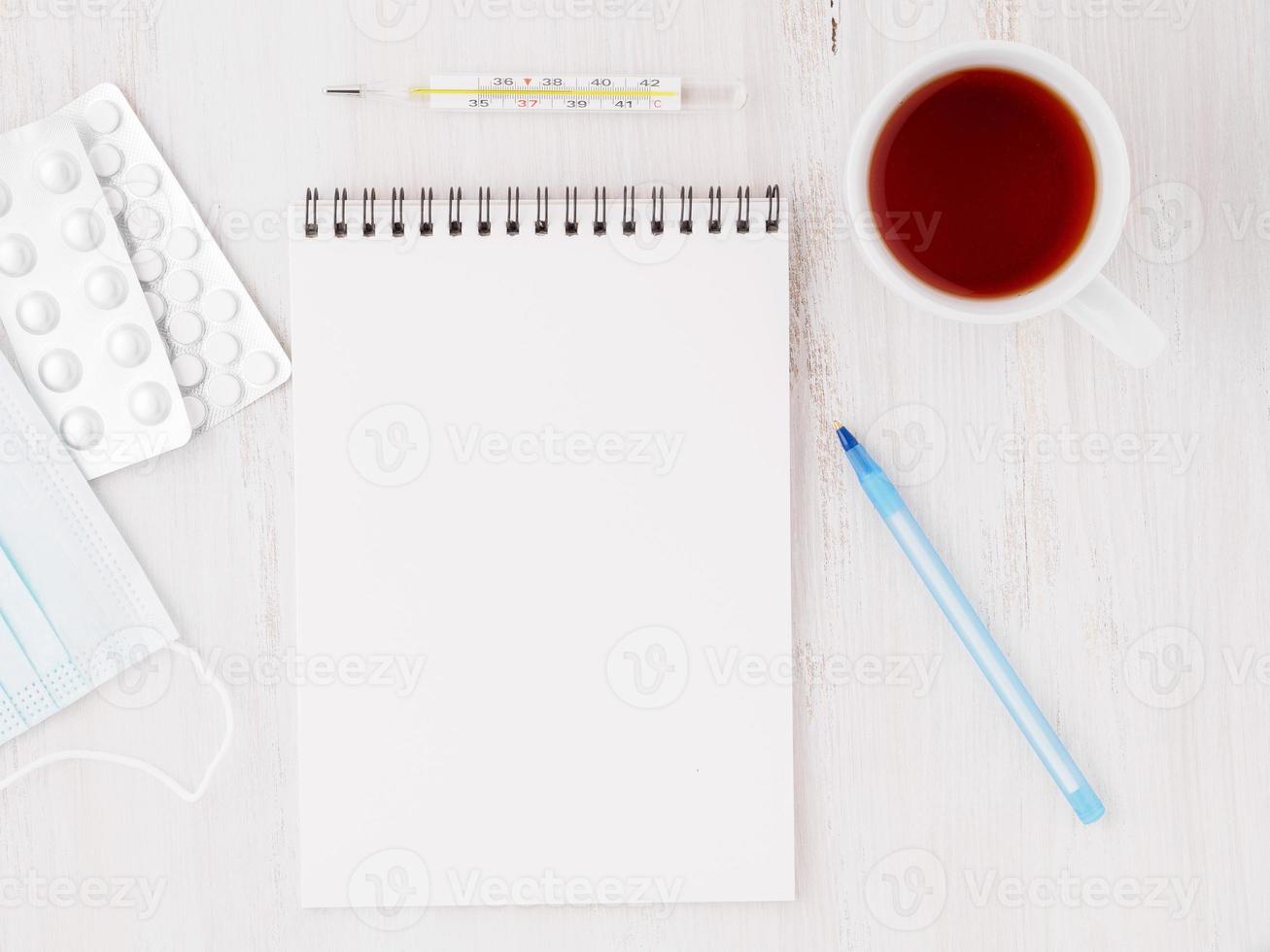 caderno aberto com página limpa branca em branco para escrever o plano de tratamento do doente. pílulas, caneta, papel, termômetro em fundo branco de madeira, vista superior. foto