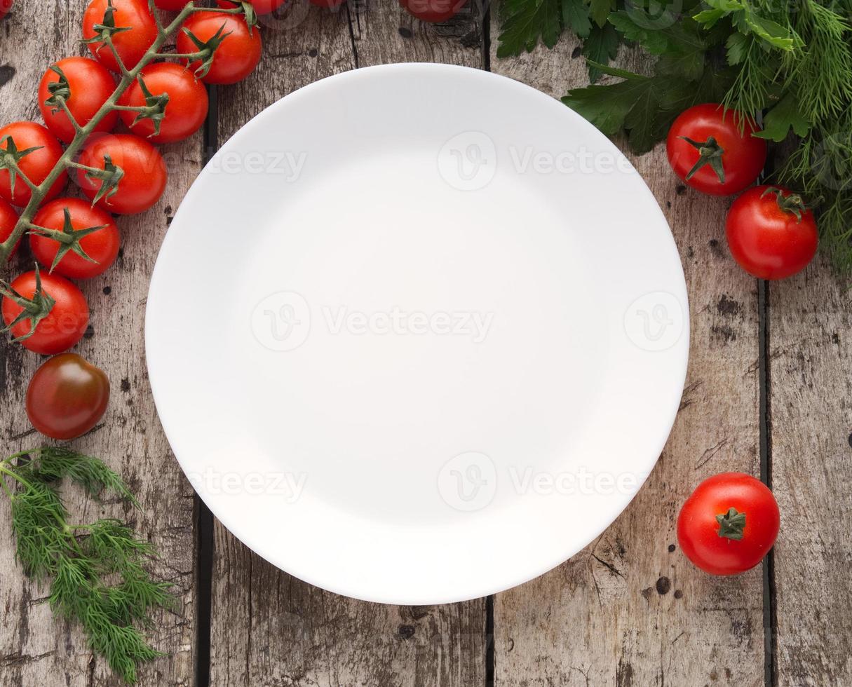 limpe o prato branco vazio e legumes, tomate, salsa no antigo fundo cinza de madeira rústica foto