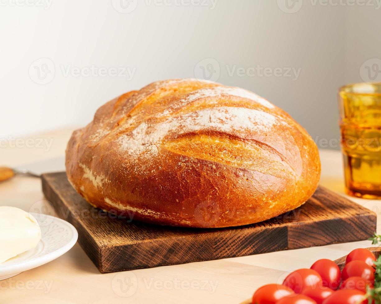 pão inteiro de trigo branco recém-assado na placa de madeira na mesa da cozinha em casa foto