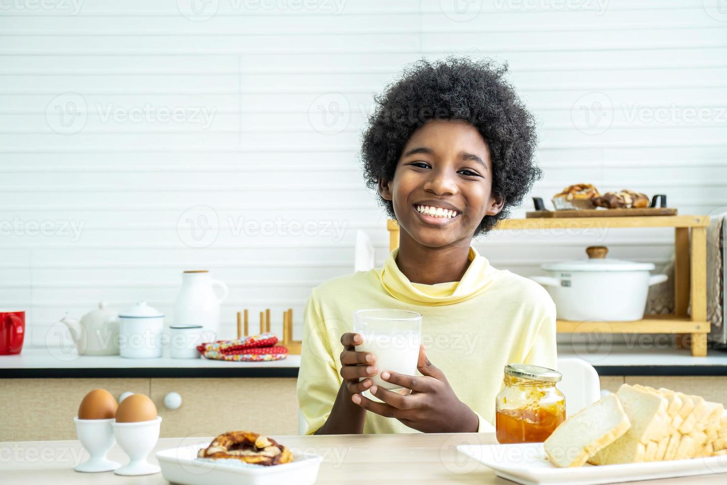 criança tomando café da manhã. feliz menino afro-americano bonito bebendo leite e comendo pão com ovo. as crianças comem na manhã ensolarada. nutrição equilibrada saudável para crianças pequenas. foto