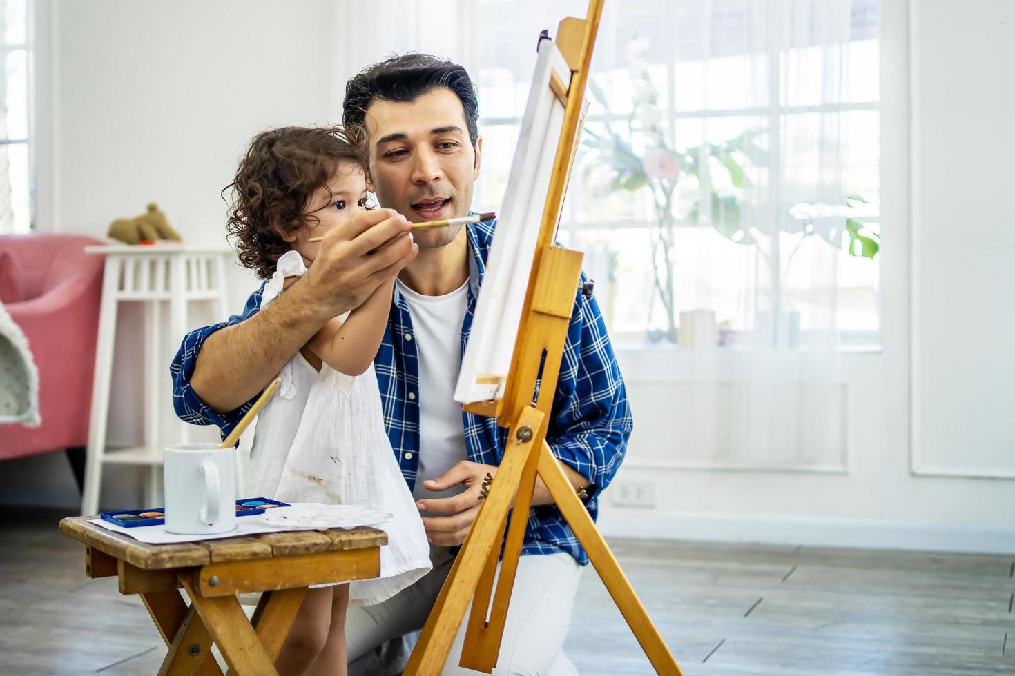 família feliz de pai e filho desenhando, usando diferentes tintas e pincéis. pai bonito e filha bonita contra imagens de óleo sorrindo, se divertindo. lição de arte foto