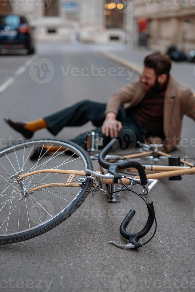 acidente de bicicleta na cidade. ciclista de homem caiu de bicicleta de estrada enquanto andava de bicicleta. lesão de bicicleta, joelho ferido foto