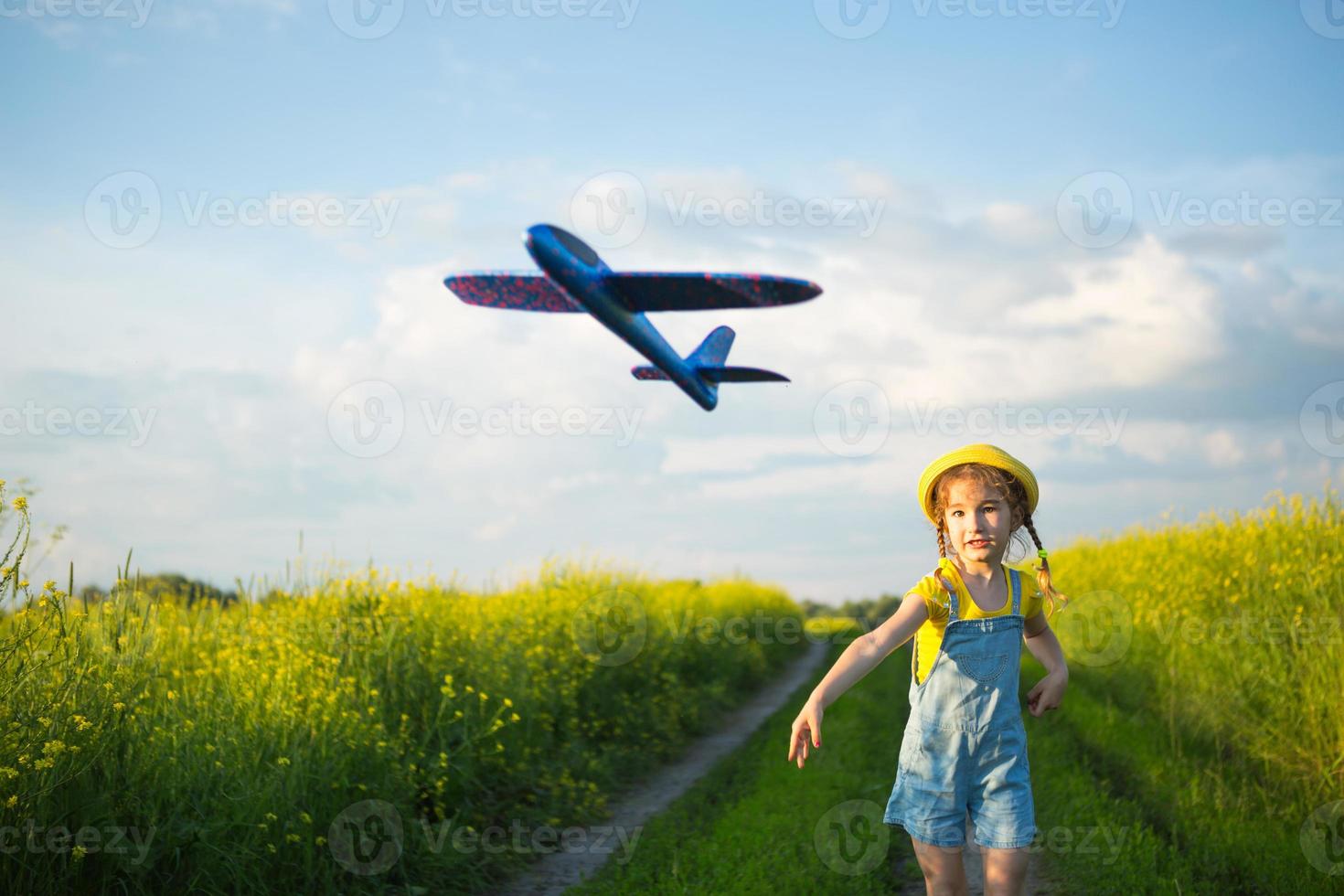 garota de chapéu panamá amarelo lança um avião de brinquedo para o campo. horário de verão, infância, sonhos e descuido. tour aéreo de uma agência de viagens em uma viagem, aventura e férias. aldeia, núcleo de casa de campo foto