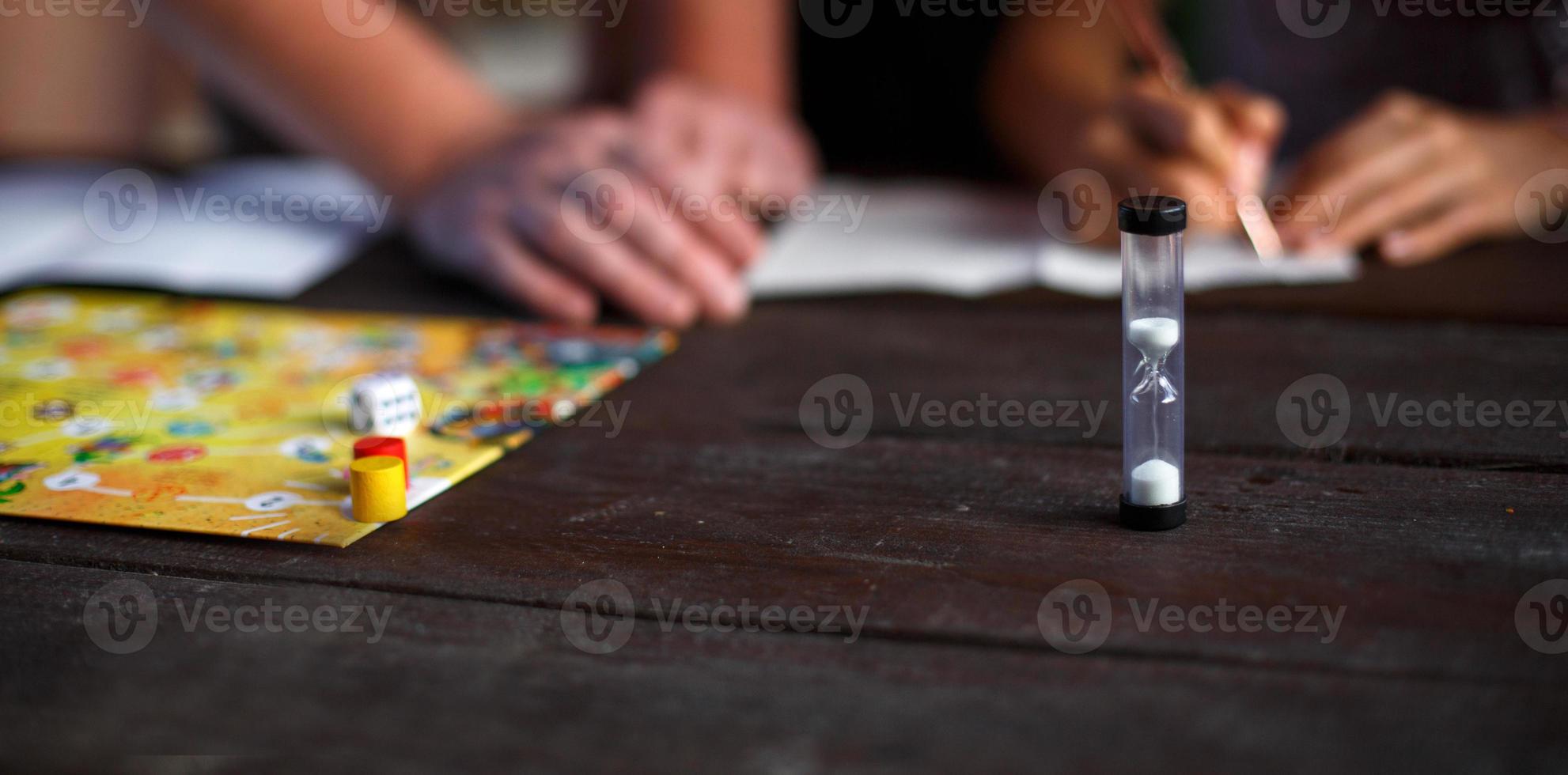 tabuleiro de jogo de tabuleiro, batatas fritas, cubo, temporizador em uma mesa de madeira escura e mãos ao fundo. o conceito de trabalho em equipe, relaxamento intelectual, evento corporativo, brincar em casa com as crianças. espaço de cópia foto